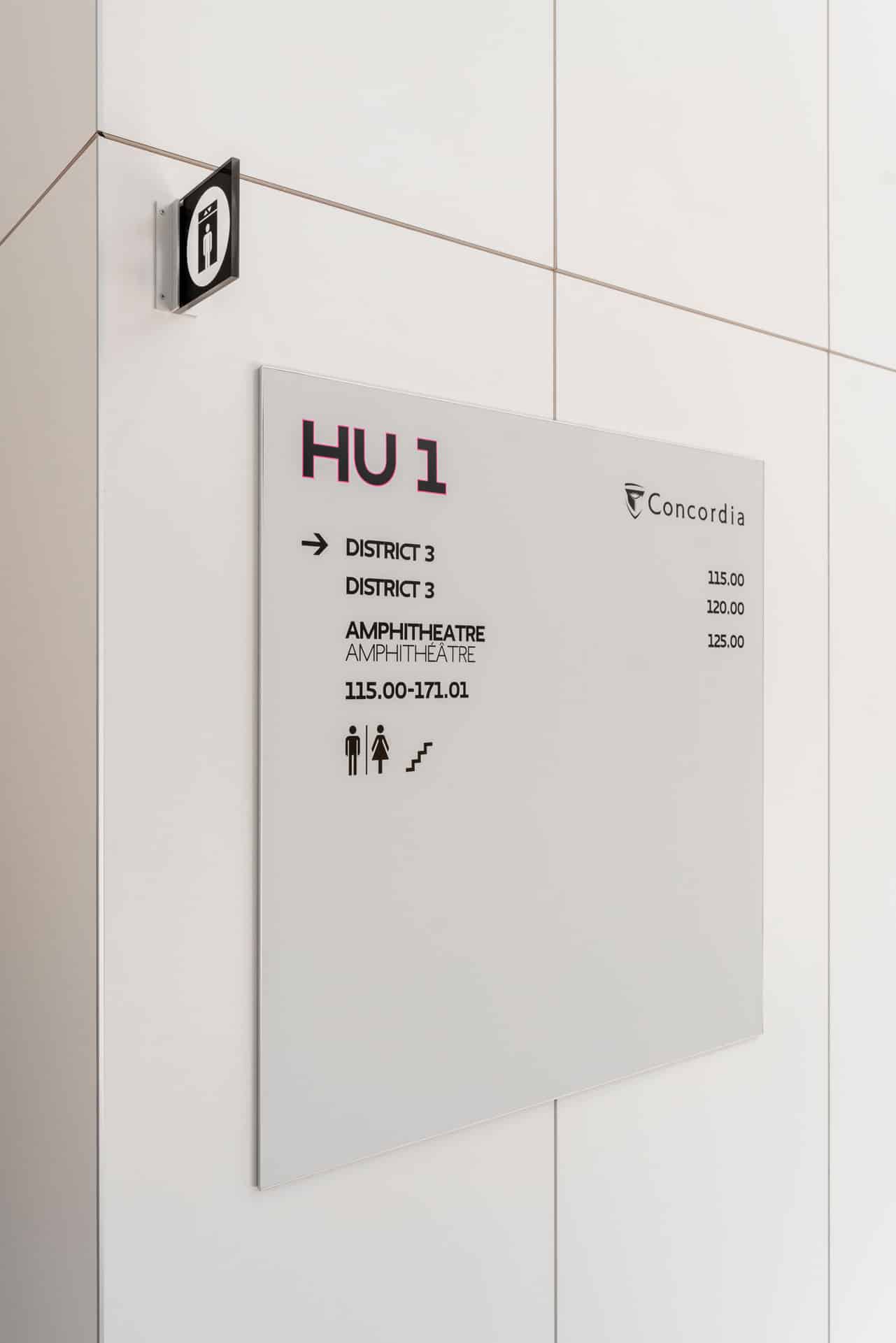 Arium Design - Directionnel mural et en potence orientant vers les ascenseurs et les autres services du niveau 1 du HUB de l'Université Concordia.